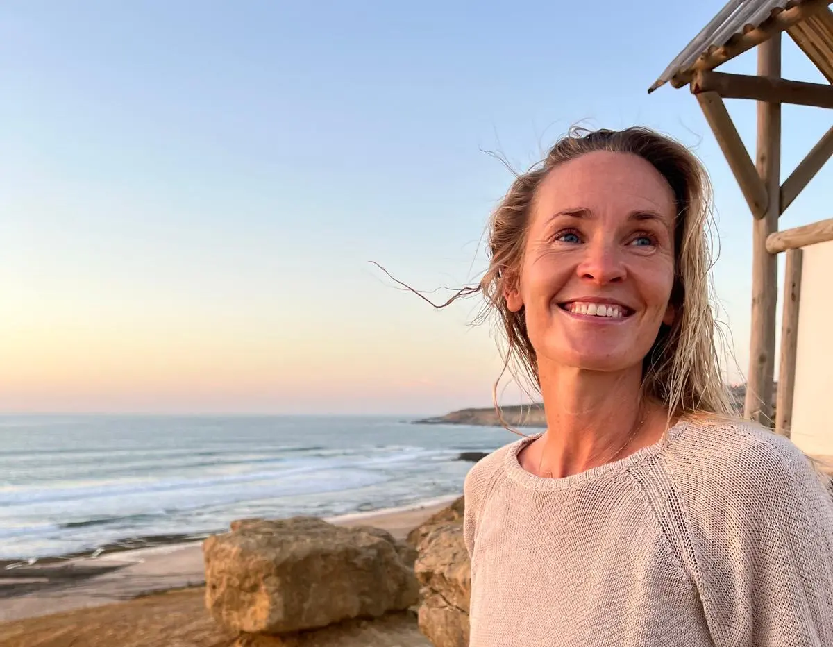 lady at beach with smiling with waves in the background. The colours are blues, yellows and pink